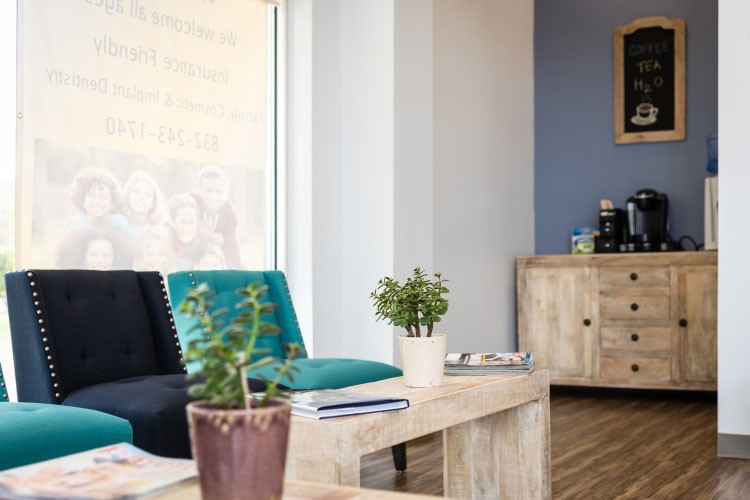 The image shows an interior space that appears to be a waiting area or reception, with a modern design featuring a blue wall, a wooden cabinet, a green chair, and some decorative items.