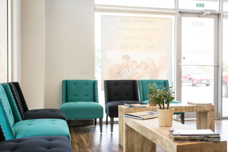 The image shows a modern waiting area with blue and green furniture, a neutral color palette, and a clean, contemporary design.