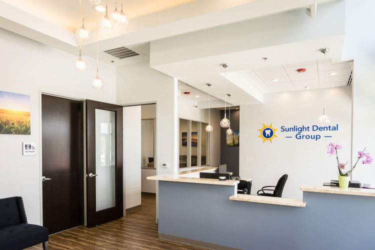 An interior view of a dental office with a reception desk, waiting area, and a sign that reads  SUNLIGHT DENTAL.