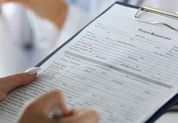 An individual is holding a clipboard with a form, which appears to be related to medical or health services, specifically patient information.