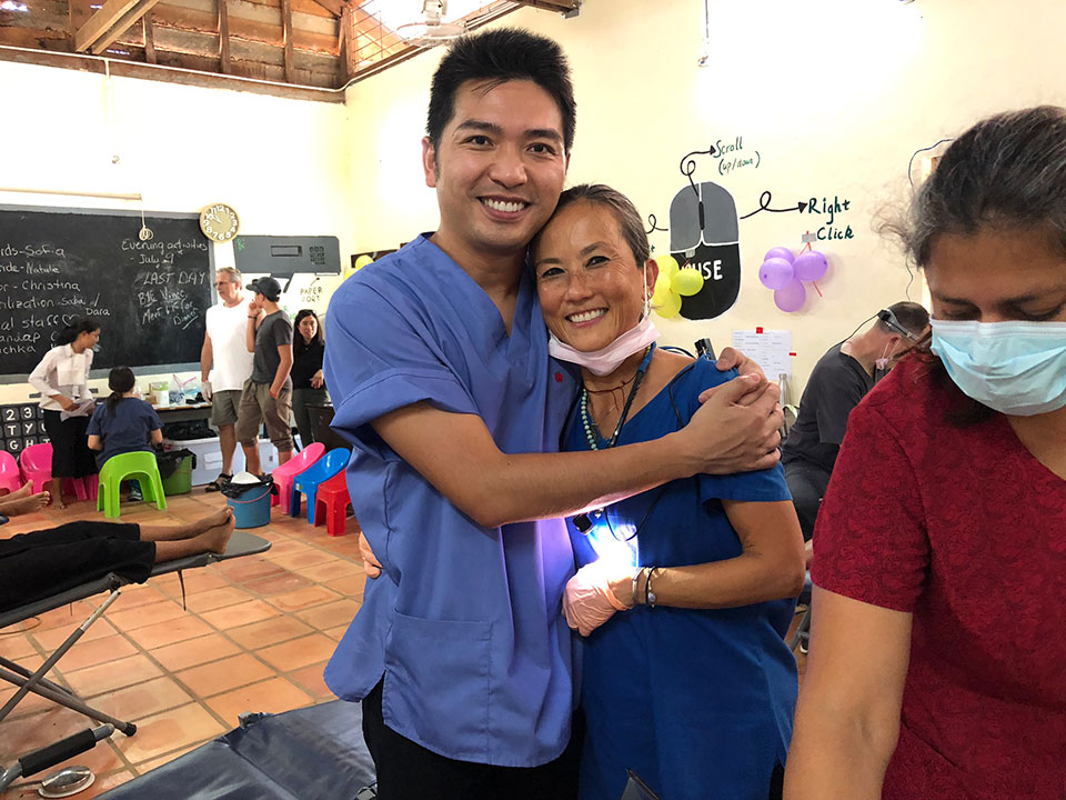 The image depicts a man and a woman in a room with medical equipment, one of them wearing scrubs, indicating they are in a healthcare setting.
