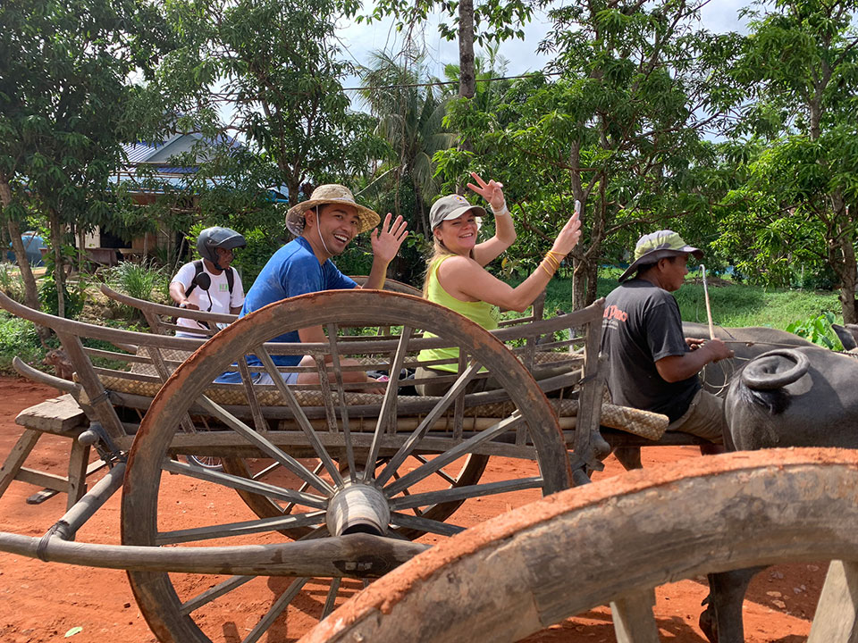 A man and woman riding in a traditional wooden cart, with the man waving to the camera.