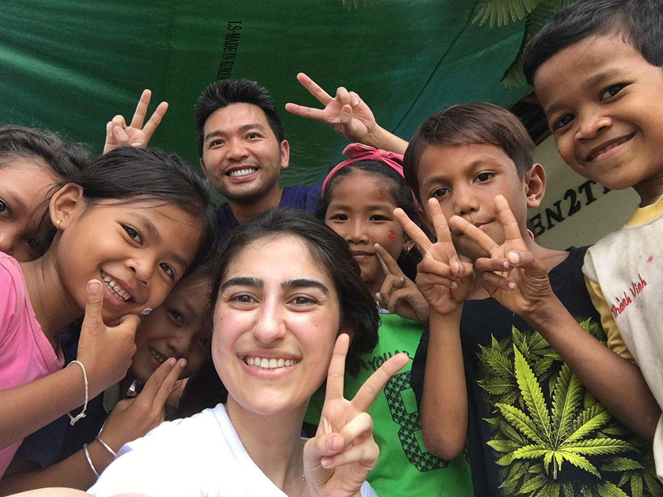 A group of children and adults, some giving peace signs, gathered under a tent.
