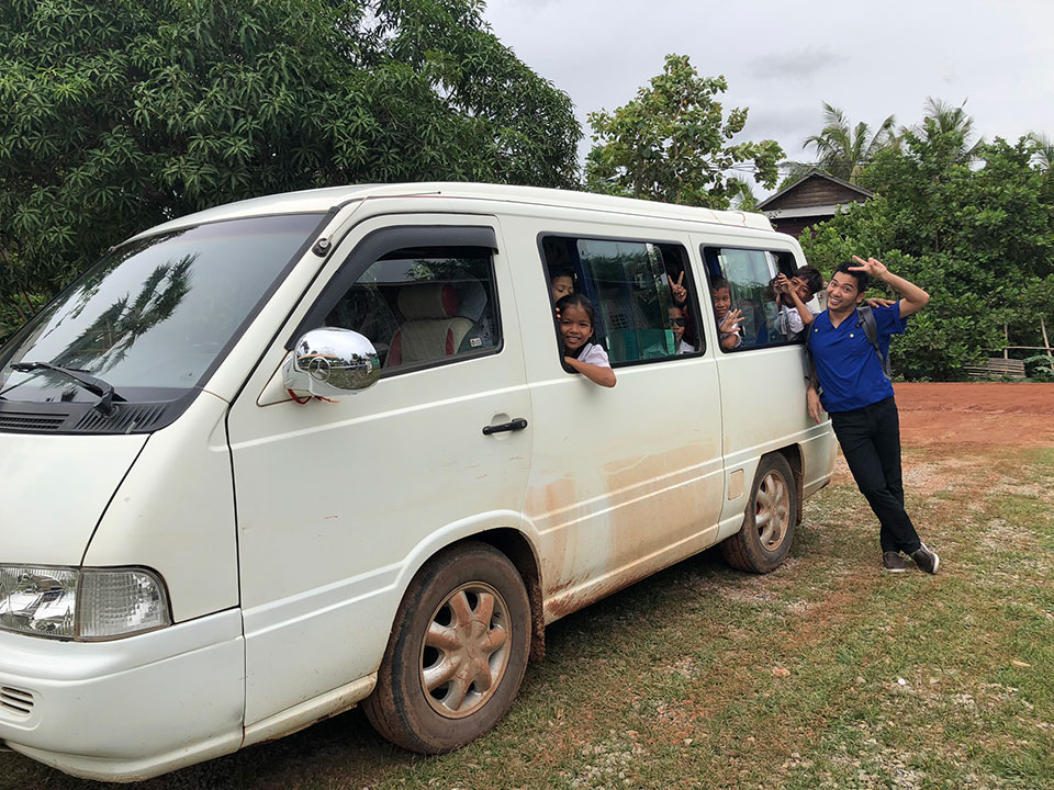 The image features a white van with multiple passengers inside, parked on a dirt road.