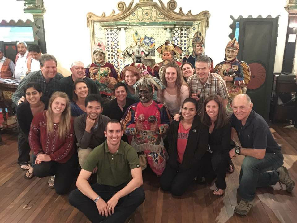 The image shows a group of people posing for a photo in front of a decorated backdrop, which includes traditional and colorful elements.