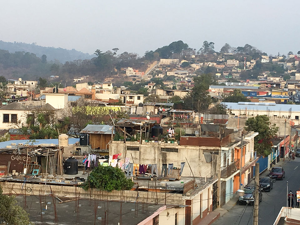 The image depicts a densely populated urban area with a mix of residential buildings and informal settlements, featuring narrow streets, corrugated metal roofs, and various types of structures.