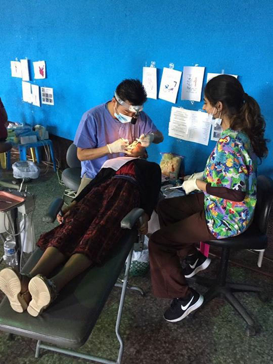 A medical professional performing a dental procedure on a patient in an improvised setting.