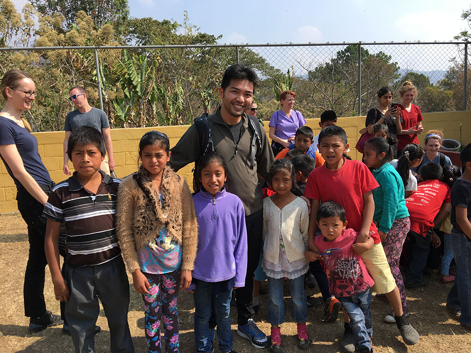 A man and a group of children pose for a photo at an outdoor event, with the man standing behind the children.