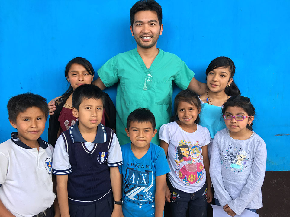 The image shows a group of children posing with an adult, likely in a school setting, with the adult possibly being a teacher or staff member.