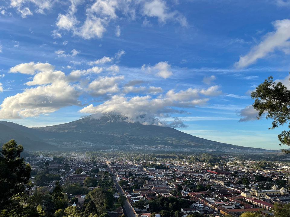The image shows a majestic mountain with a cloudy sky in the background, viewed from a high vantage point overlooking a city.