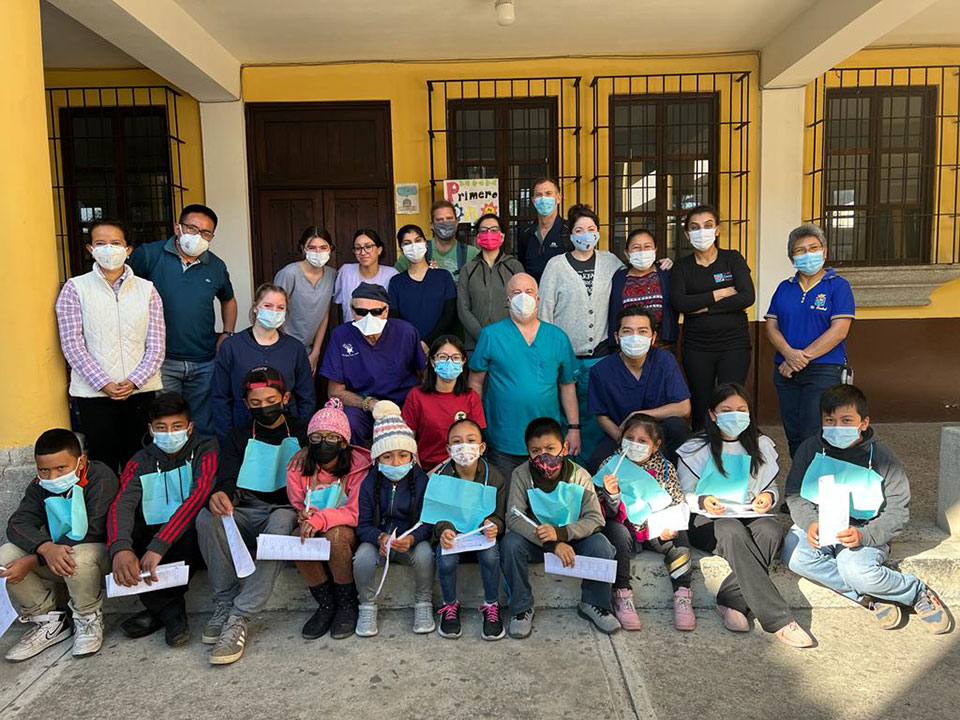 A group of people, some wearing masks and others not, gathered in front of a building with signs, posing for the photo.