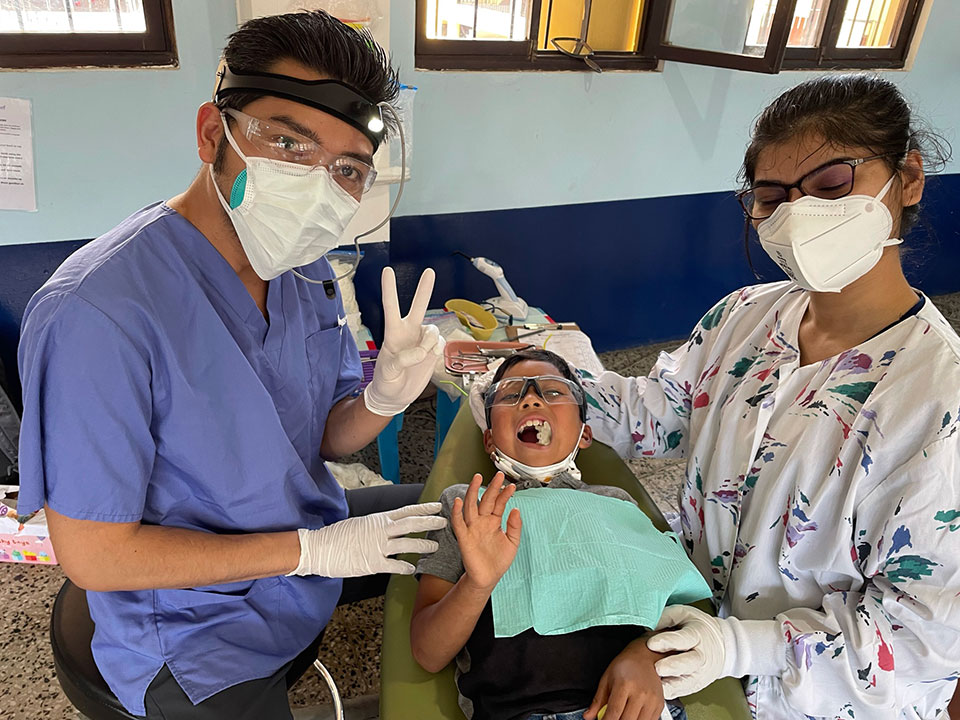 Medical personnel in a hospital setting, performing dental care on a patient with gloved hands and protective equipment.