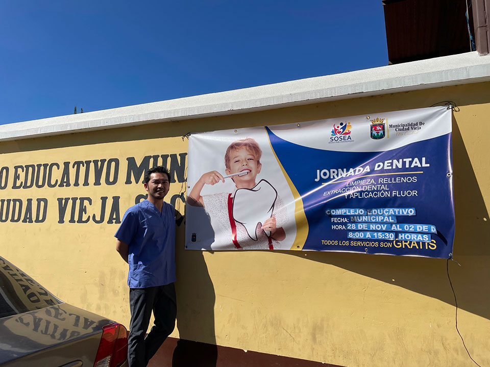 A person stands in front of a sign advertising dental services, with a banner featuring an image of a smiling dentist.