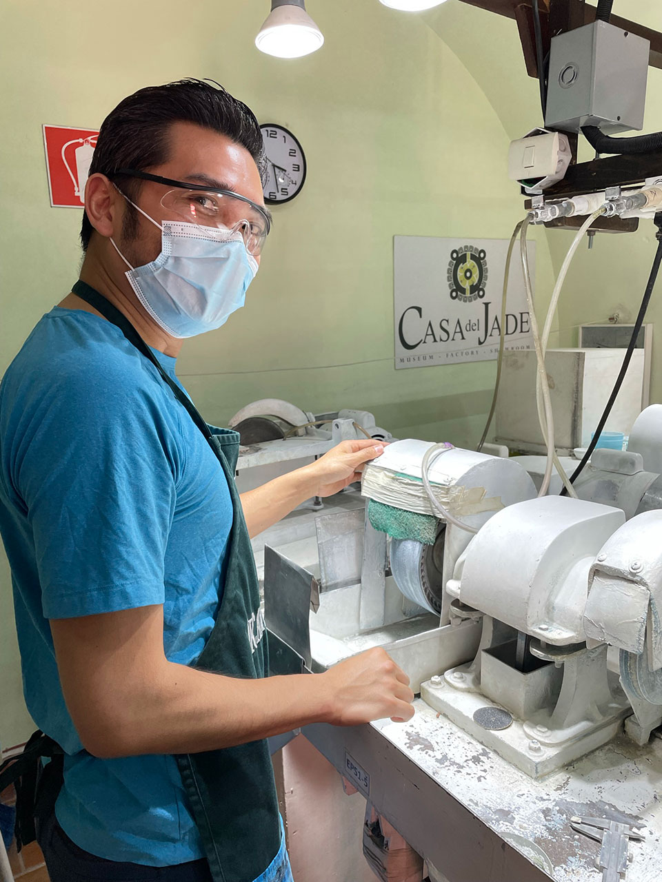 A man in a blue shirt and safety mask is operating machinery, likely in a workshop or factory setting.