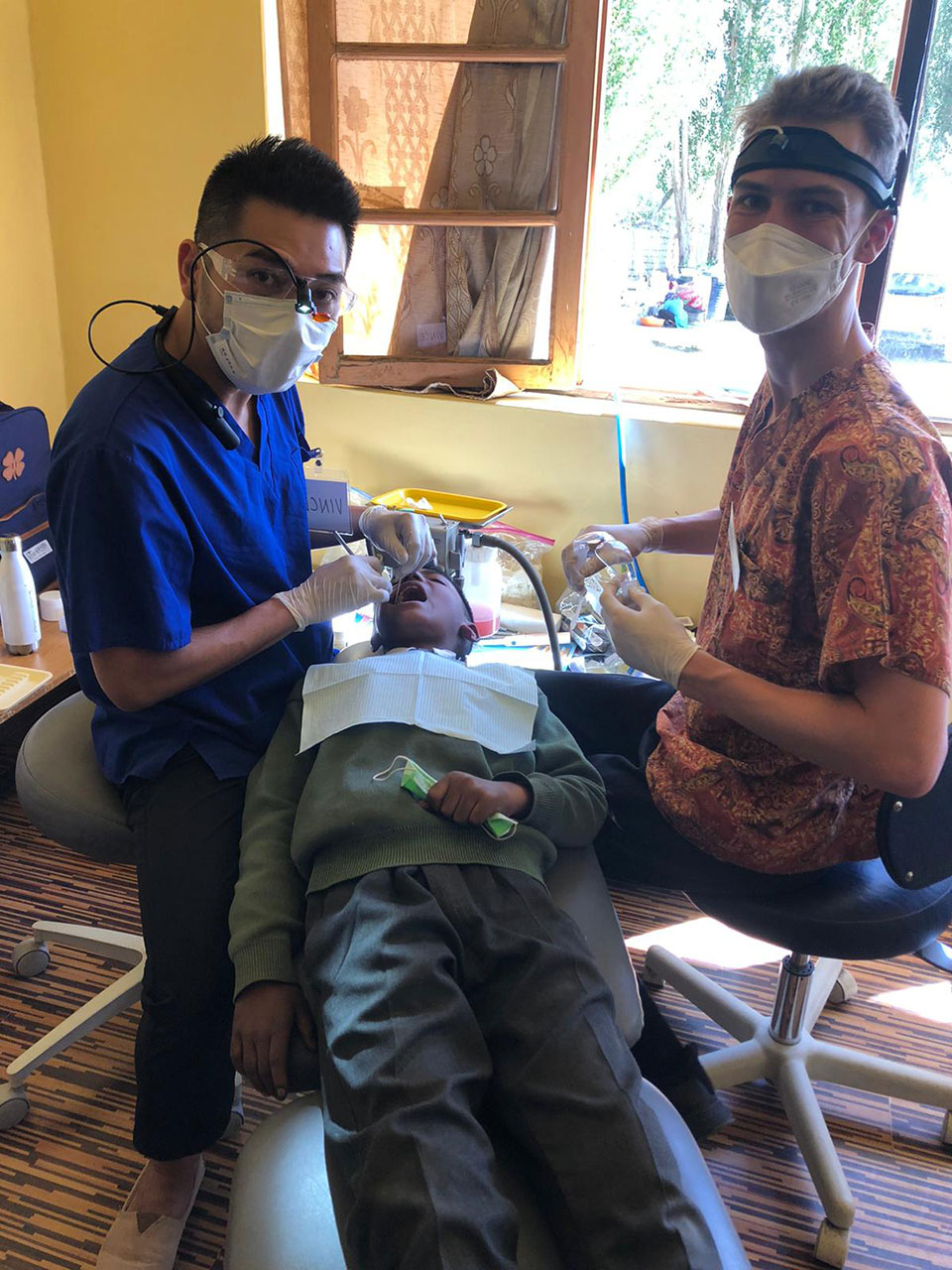 A dental clinic scene with a dentist, dental hygienist, and patient, featuring dental equipment and tools.