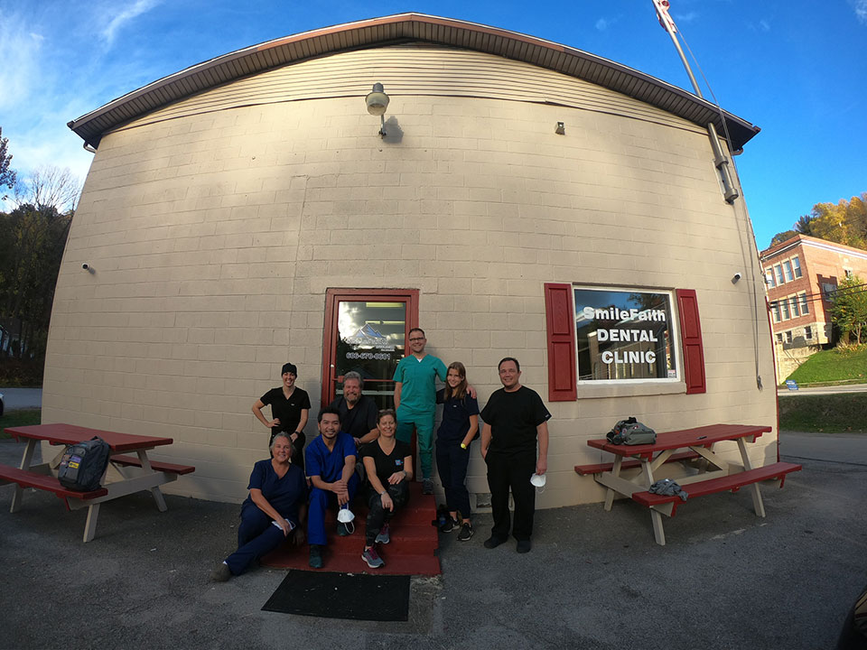 A group of individuals posing in front of a dental clinic, with a sign indicating it's an emergency dental facility.