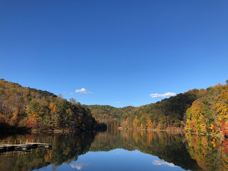 The image shows a serene landscape with a calm river reflecting the surrounding trees, under a clear blue sky.