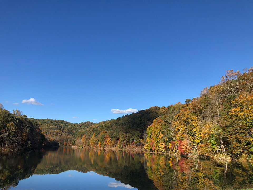The image shows a serene landscape featuring a calm river reflecting the surrounding trees, with autumnal colors visible in the foliage.