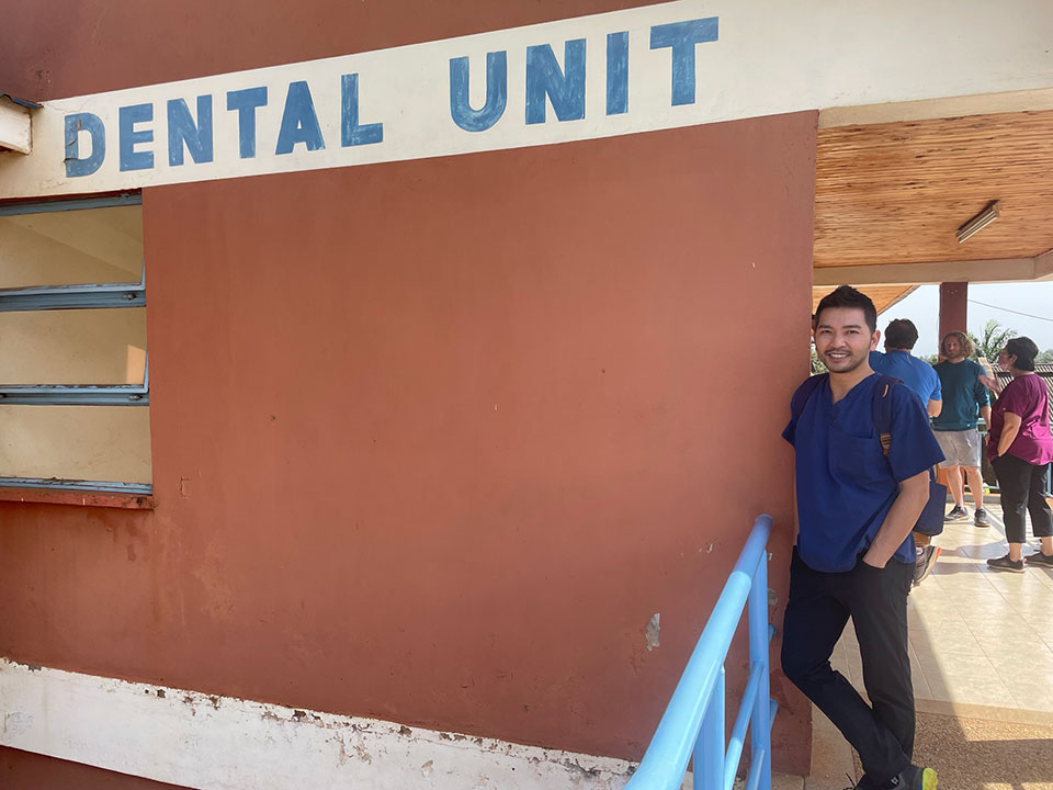 The image is a photograph of a person standing in front of a sign that reads 'DENTAL UNIT' on the exterior of a building.