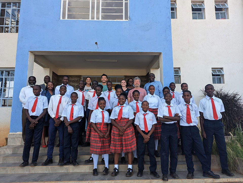 A group of people, possibly school students or a team, posing in front of a building with a blue wall.