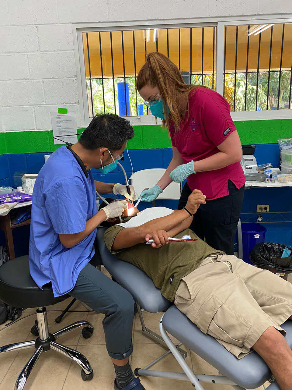 In the image, a dental professional is performing a procedure on an individual who appears to be receiving treatment in a dental chair.