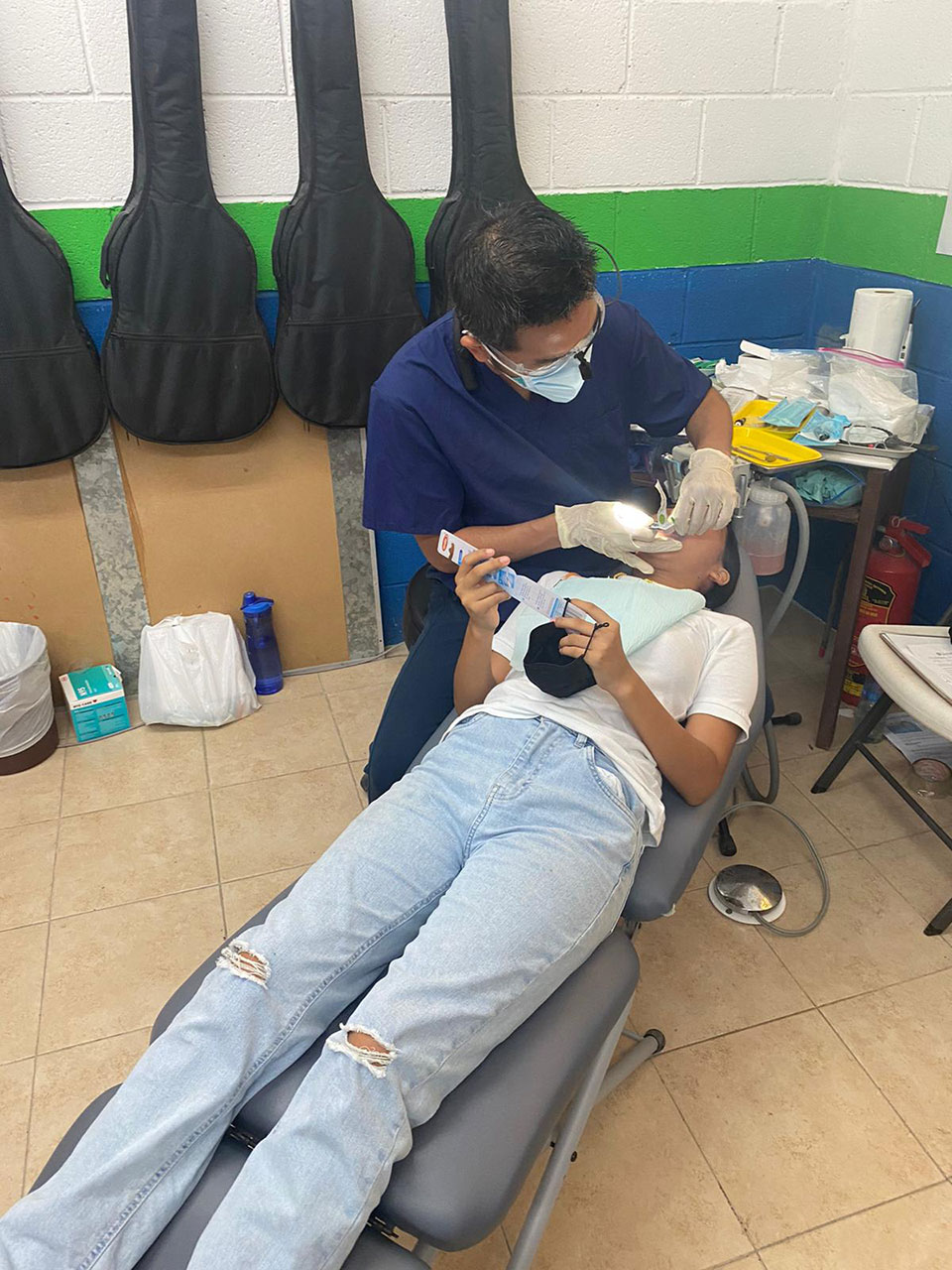 A dental hygienist in a professional setting, performing a cleaning procedure on a patient's teeth, with the patient seated in a dental chair.