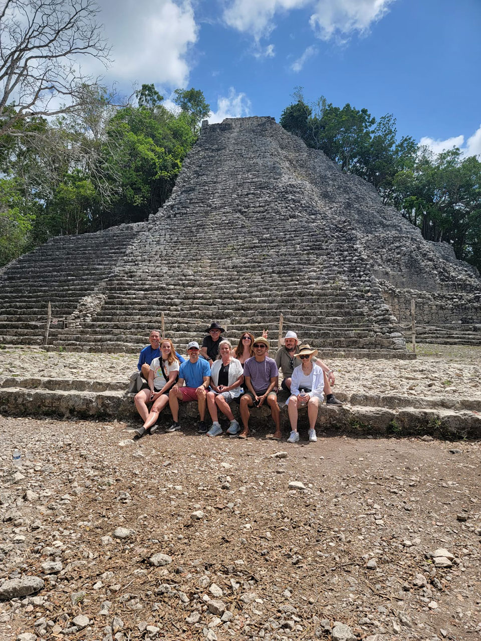 Alt' tag: A group of people posing in front of an ancient pyramid-like structure, likely a significant archaeological site.