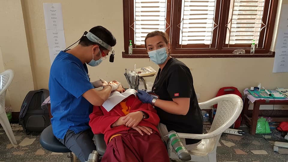 A medical professional is performing a procedure on a patient, with the assistance of another individual, in an indoor setting.
