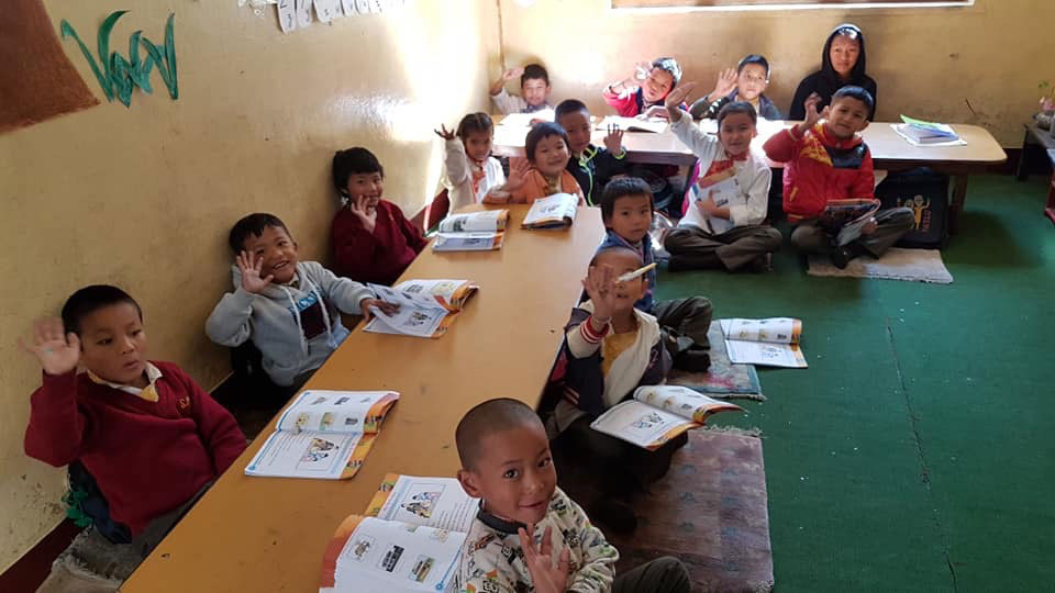 The image depicts a group of children seated at desks in a classroom, engaging with educational materials.