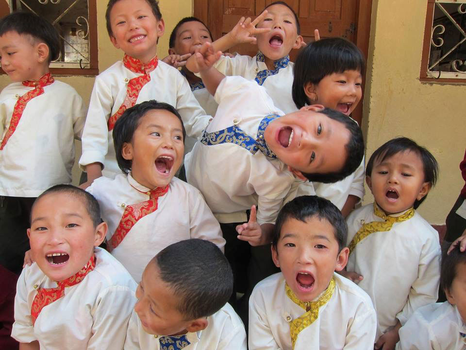 The image is a collage of several photos featuring young children, predominantly boys, wearing traditional Asian attire with red ties and blue scarves. They are smiling and appear to be in a joyful mood, possibly posing for a group photo or participating in a cultural event.