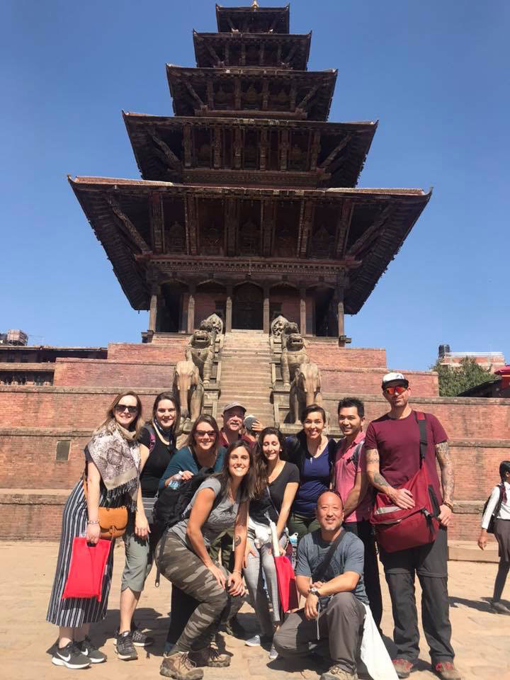 A group of people posing in front of a large, traditional multi-tiered pagoda-style building with intricate architectural details.