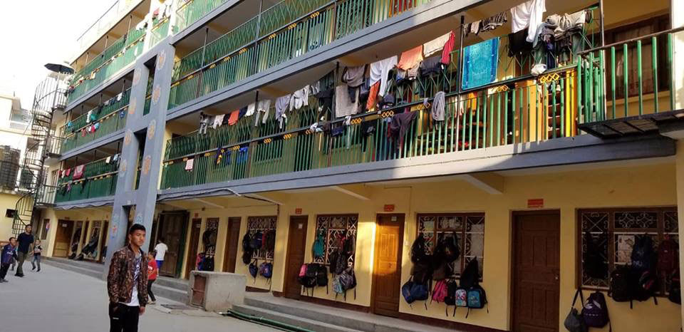 The image depicts a multi-story building with an exterior balcony, where clothing is hanging to dry.