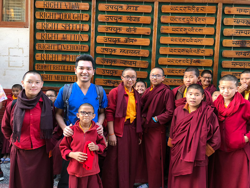 A group of people, including a man in a blue shirt and a child, posing for a photo with a signboard displaying text and numbers behind them.
