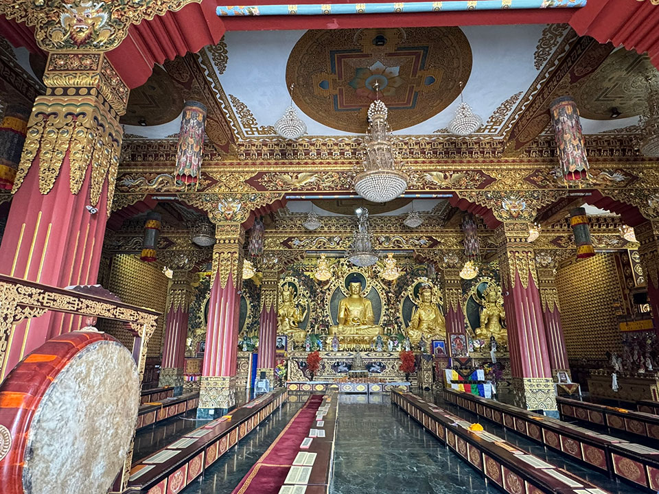 The image shows an interior view of a large, ornate temple with multiple tiers of seating and decorative elements.