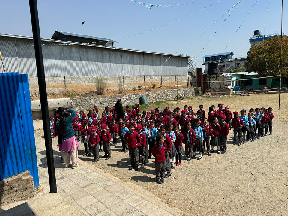 An outdoor scene with a group of children in school uniforms, standing on a dirt ground, facing the camera.