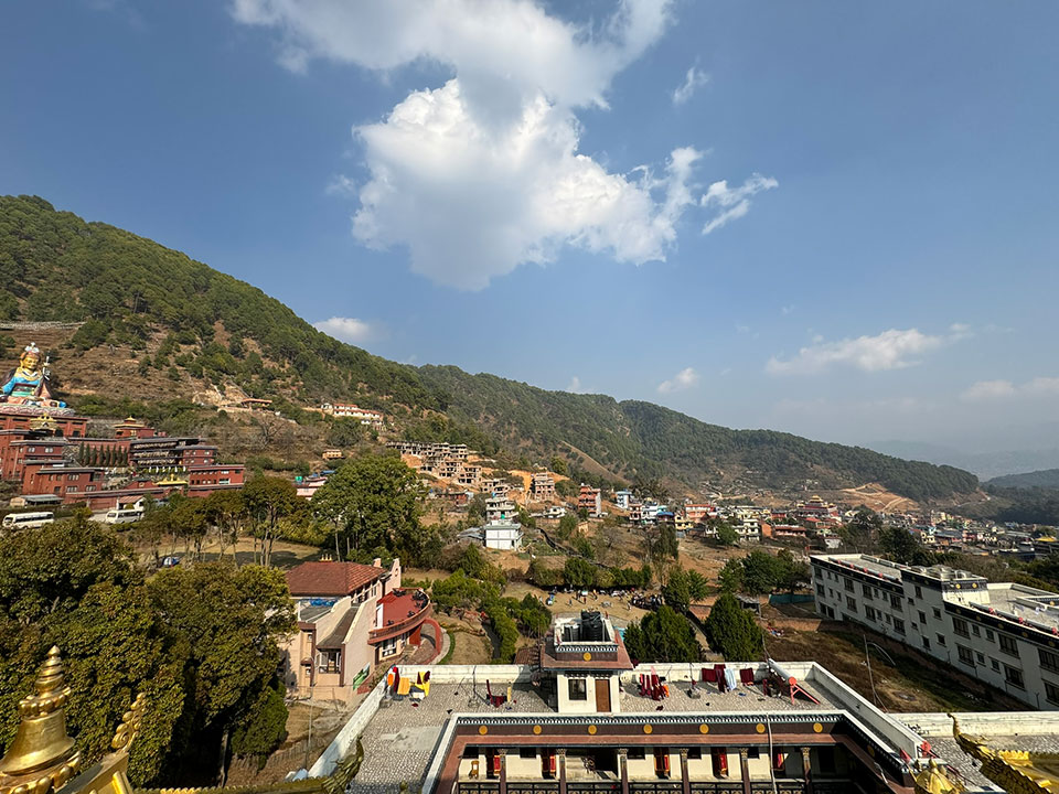 The image depicts a picturesque mountainous village with traditional architecture, set against a clear sky with scattered clouds.