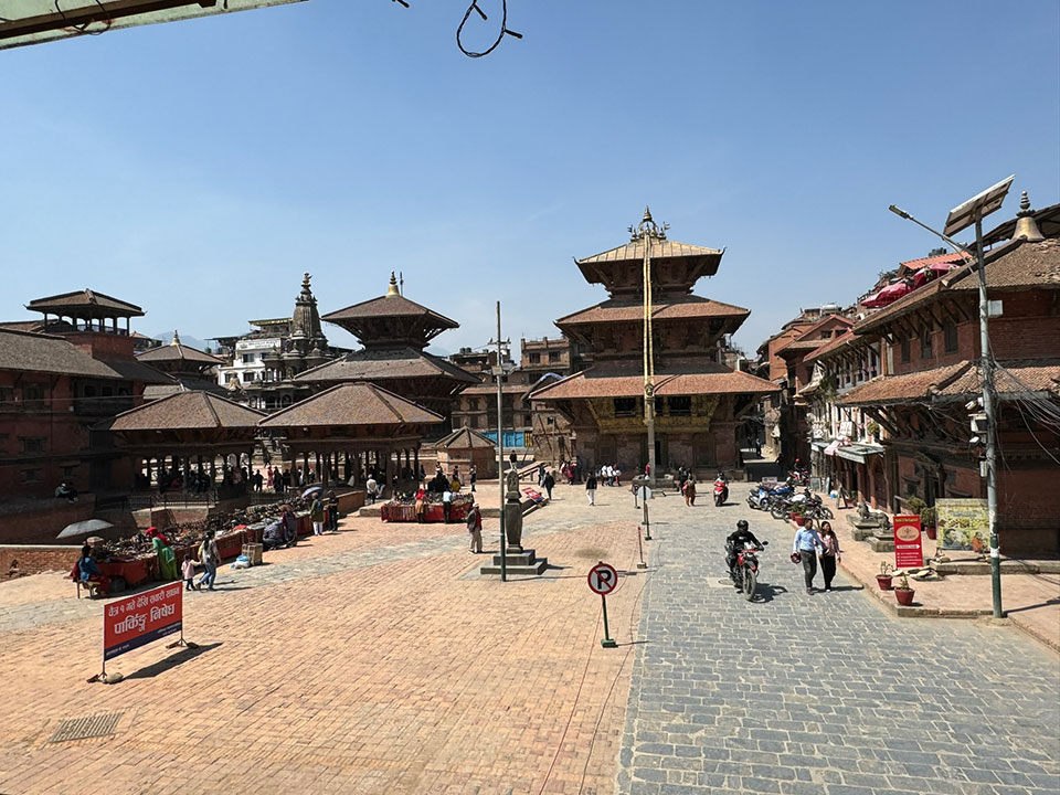 The image depicts an urban scene in a South Asian city, with traditional architecture and a bustling street.