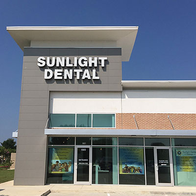 The image shows a sign for  Sunlight Dental  in front of a building with a clear sky and no visible people.