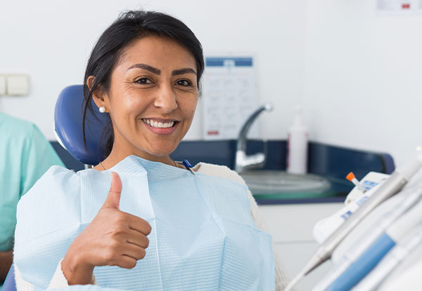 A dental hygienist wearing a surgical mask and giving a thumbs-up gesture.