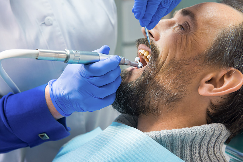 In the image, a dental professional is performing an oral procedure on a patient using specialized equipment.