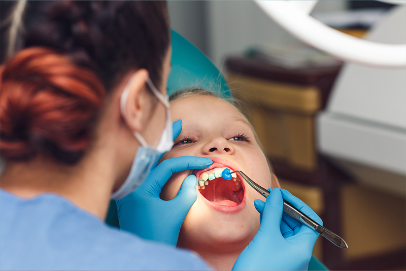 A dentist is performing a dental procedure on a patient, with the patient seated in a dental chair and wearing a surgical mask.