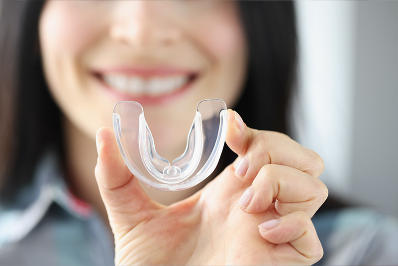 A smiling woman holding a clear plastic dental impression mold.