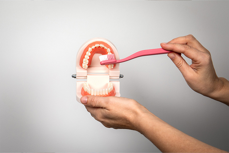The image shows a person s hand holding a toothbrush near a transparent model of a mouth with teeth, suggesting the demonstration or use of an electric toothbrush.