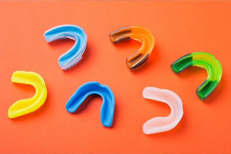 The image displays a collection of colorful hearing aid ear molds against a light red background.