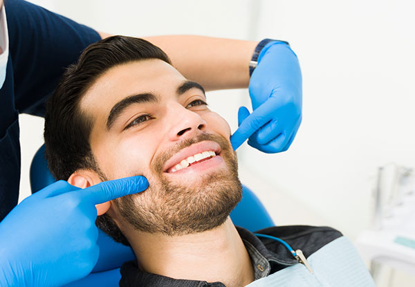 A man in a dental office chair, receiving teeth straightening treatment with a smile on his face.