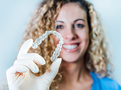 A woman in a blue shirt holds up a large, transparent dental retainer with a smile.