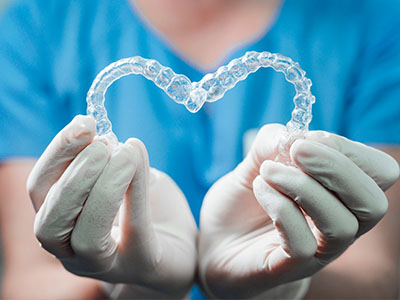 An individual in a blue uniform, wearing gloves and holding a transparent heart-shaped dental appliance.