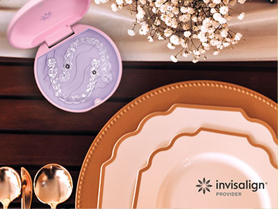 Image displays a collection of tableware on a wooden surface, including plates, bowls, and a pink toothbrush holder with a patterned lid, set against a blurred background with decorative elements.
