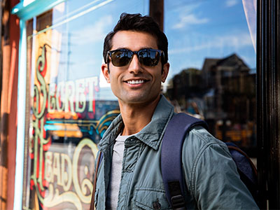 A man in sunglasses, a jacket, and a backpack stands confidently outside a shop with a sign that reads  Sinbad s.