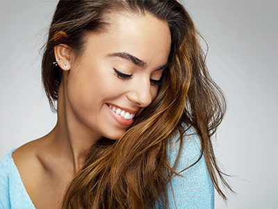 A young woman with long hair, smiling and looking downwards.